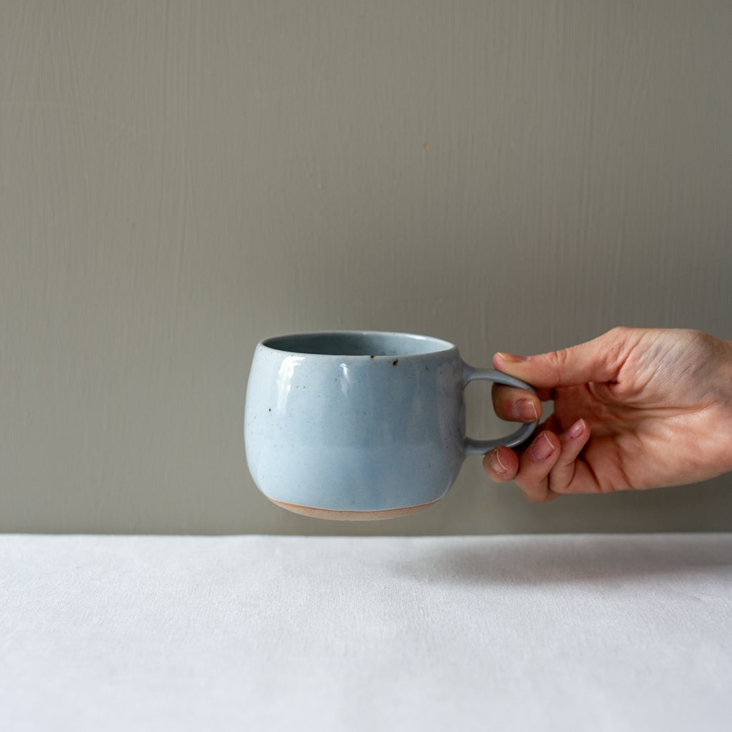 Hand holding a handmade Palinopsia coffee mug in blue speckle 