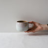 Hand holding out a single handmade mug in white, chocolate and pink colours