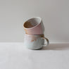 A stack of coffee cups and mugs by Palinopsia Ceramics in pinks, browns and white