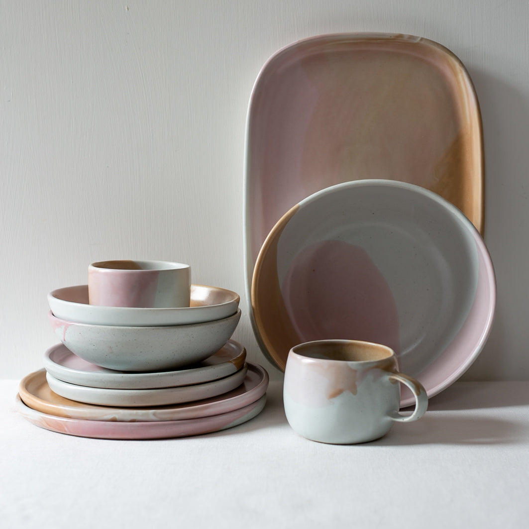 Handmade tableware by Palinopsia Ceramcis stacked against a white background, dinner plates, lunch plates, breakfast bowls, mugs, cups, platters, salad and a fruit bowl  
