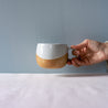 A hand holding out a handmade mug by Palinopsia Ceramics in blue, brown and grey