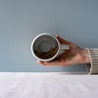 A hand holding out a mug by Palinopsia Ceramics showing the internal glazing work