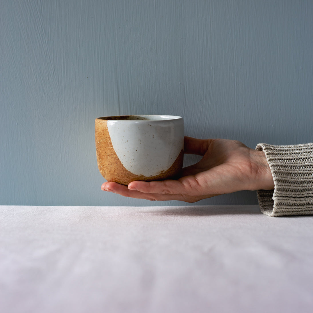 A hand holding out a handmade coffee and tea cup by Palinopsia Ceramics