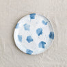 Bird's-eye view of a single Palinopsia's Dinner Plate in the coastal Pollock collection, with blue and white splatters and drippy glaze on a linen tablecloth