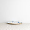 A single handmade Palinopsia dinner plate in blue and white splatter design with drippy glaze, on a white background 