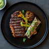 Birds-eye view of a handmade black ceramic dinner plate by Palinopsia Ceramics served with perfectly grilled steak, bone marrow and grilled vegetables by Sydney chef Gerald Touchard from the Northern Beaches 